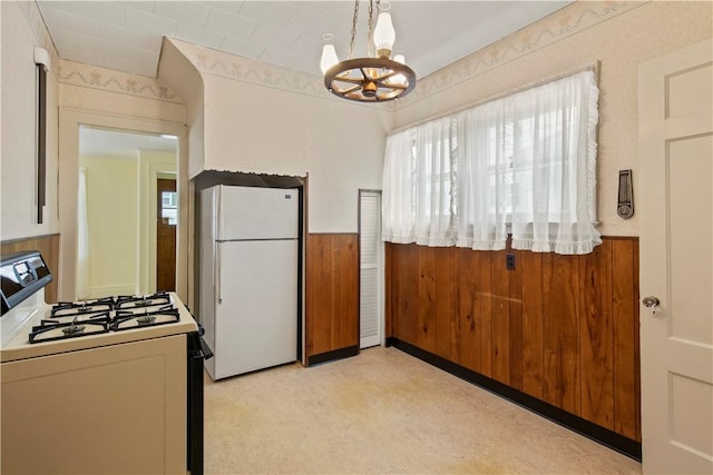 kitchen with white appliances, a wainscoted wall, wooden walls, and an inviting chandelier