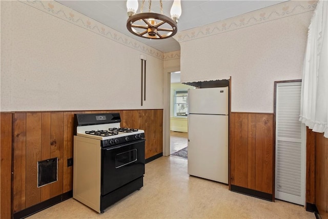 kitchen with gas stove, freestanding refrigerator, a wainscoted wall, and wood walls