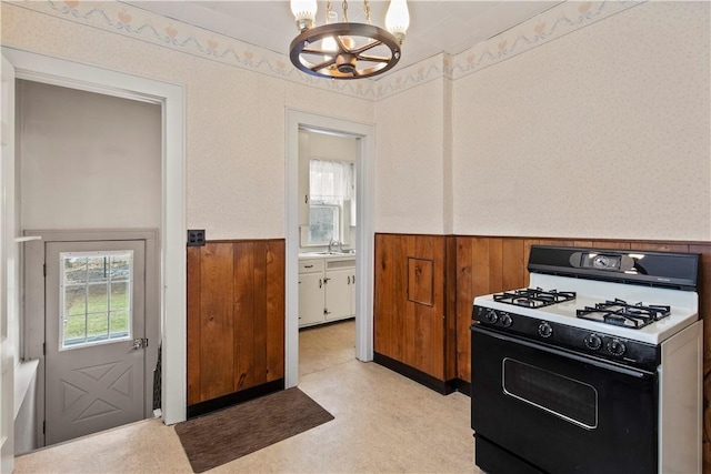 kitchen with wainscoting, range with gas cooktop, an inviting chandelier, light floors, and a sink