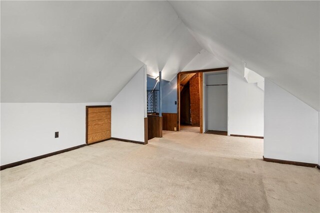 additional living space with baseboards, vaulted ceiling, and light colored carpet