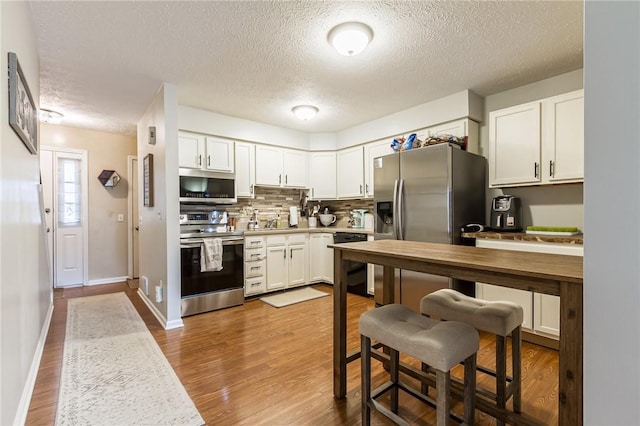 kitchen with dark wood-style floors, stainless steel appliances, light countertops, backsplash, and white cabinetry