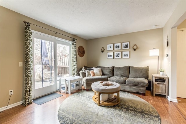 living room with light wood-type flooring, a textured ceiling, and baseboards