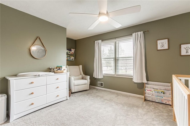 bedroom featuring a crib, baseboards, visible vents, a ceiling fan, and carpet flooring