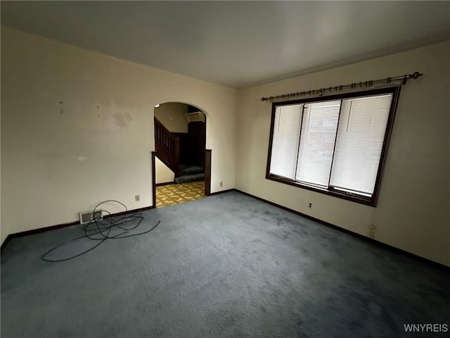 carpeted spare room with arched walkways, stairway, and baseboards