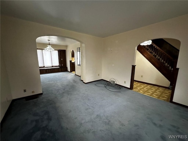 carpeted spare room featuring arched walkways, baseboards, and stairs