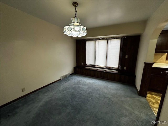 unfurnished dining area with arched walkways, carpet, visible vents, and baseboards