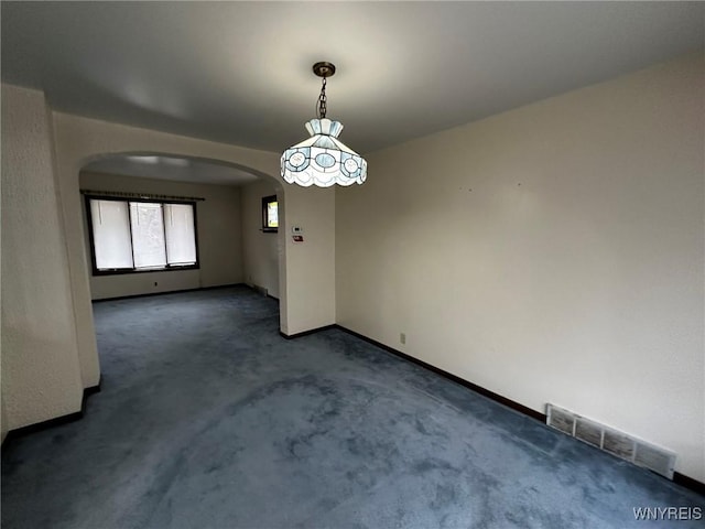 unfurnished dining area featuring arched walkways, carpet floors, visible vents, and baseboards