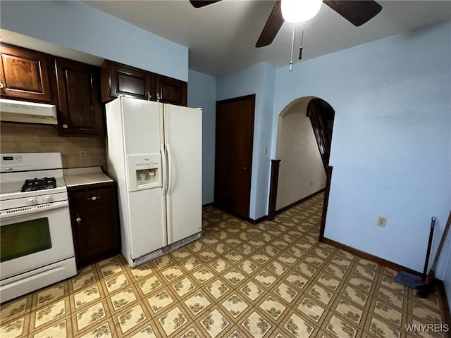 kitchen with white appliances, baseboards, arched walkways, light floors, and under cabinet range hood