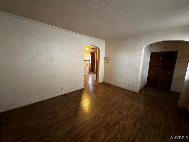 unfurnished room with baseboards, arched walkways, a textured wall, wood finished floors, and a textured ceiling