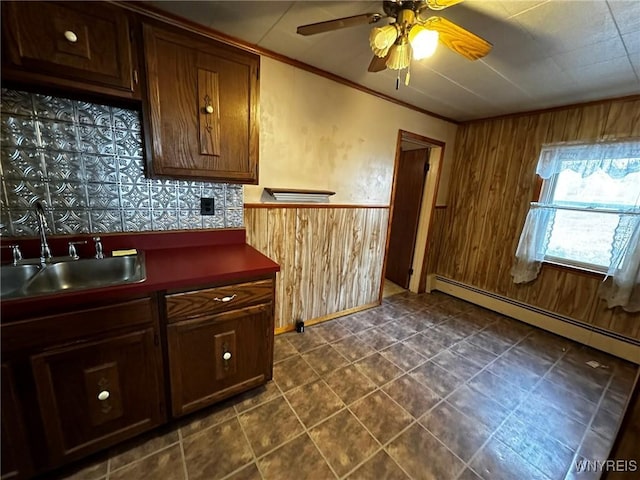 kitchen featuring a baseboard radiator, wood walls, a sink, dark countertops, and crown molding