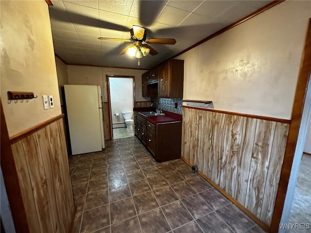 kitchen featuring a wainscoted wall, dark countertops, freestanding refrigerator, wood walls, and a sink