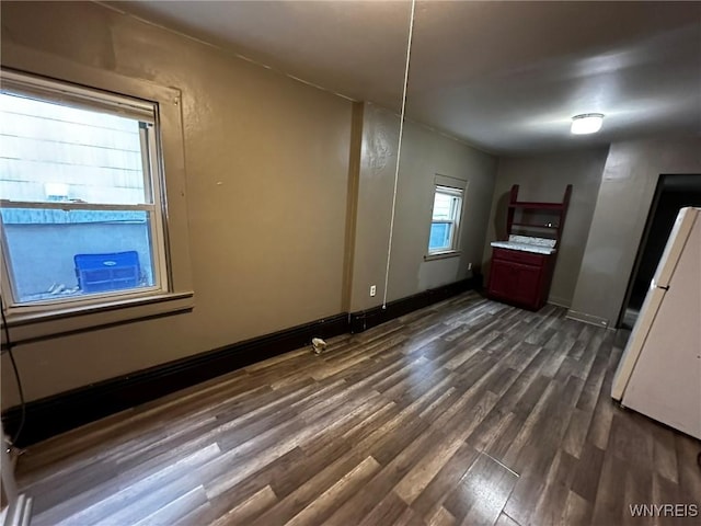 unfurnished bedroom with dark wood-type flooring, freestanding refrigerator, and baseboards