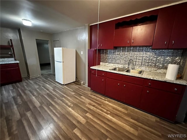 kitchen featuring red cabinetry, decorative backsplash, freestanding refrigerator, light countertops, and a sink