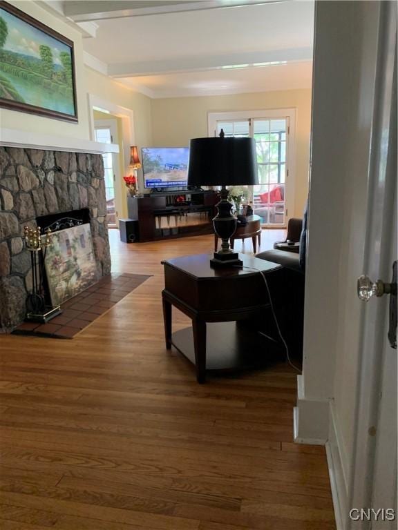 living area featuring a stone fireplace, beamed ceiling, and wood finished floors