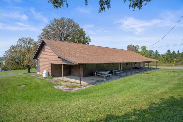 back of property featuring a shingled roof, a patio area, a yard, and a chimney