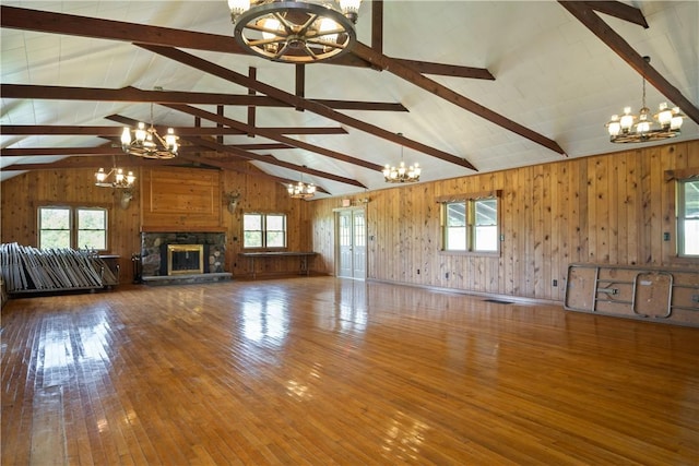 unfurnished living room featuring wood-type flooring, an inviting chandelier, wood walls, a stone fireplace, and beamed ceiling