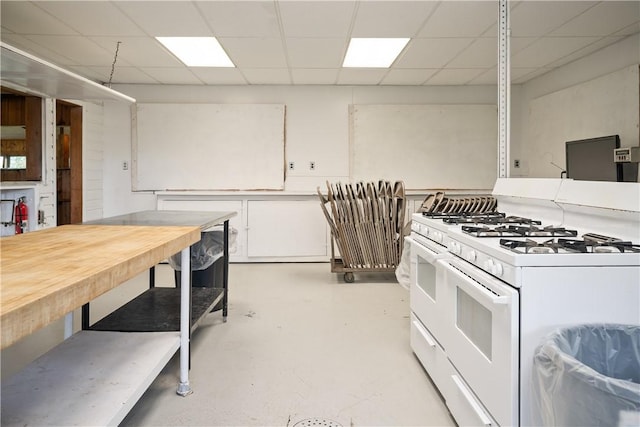 kitchen featuring a drop ceiling, white gas range oven, white cabinetry, and finished concrete floors