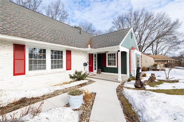 view of exterior entry with a shingled roof, brick siding, and board and batten siding