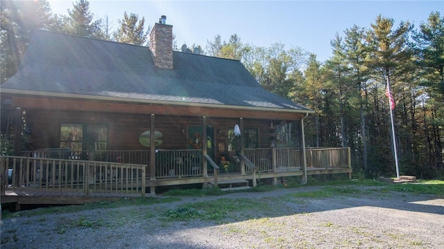 rear view of property featuring roof with shingles, a porch, and a chimney