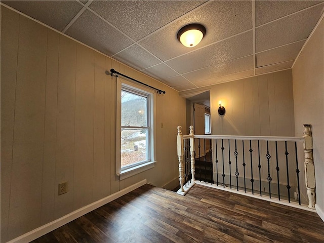 unfurnished room with baseboards, a drop ceiling, and dark wood-style flooring