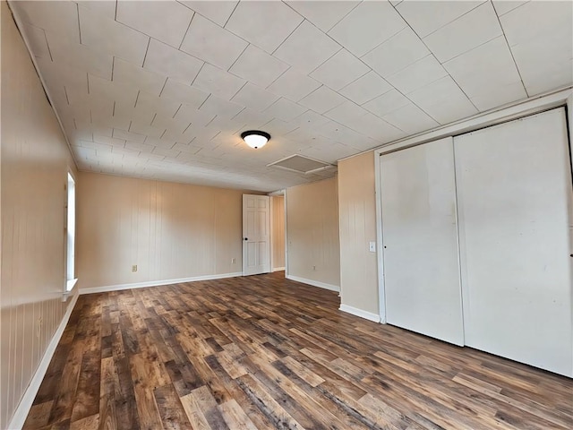 unfurnished bedroom with a closet, wood finished floors, attic access, and baseboards