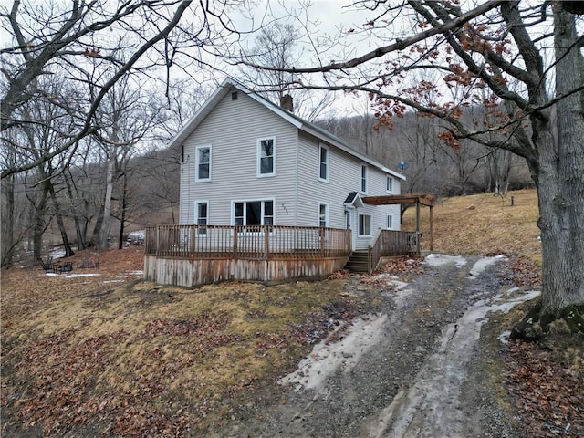 view of side of home featuring dirt driveway, a chimney, and a wooden deck