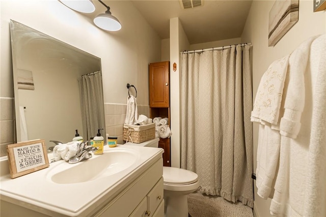 bathroom featuring toilet, vanity, visible vents, and tile walls