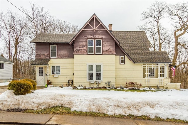 snow covered house featuring a shingled roof and a chimney