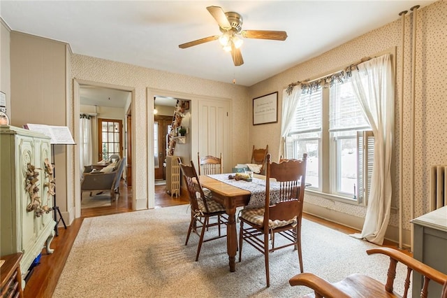 dining room featuring wood finished floors, a ceiling fan, and wallpapered walls