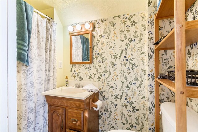 bathroom with toilet, wallpapered walls, a textured ceiling, and vanity