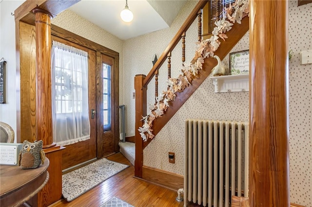 foyer entrance with hardwood / wood-style flooring, wallpapered walls, radiator heating unit, baseboards, and stairs