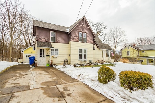 snow covered property with driveway and roof with shingles