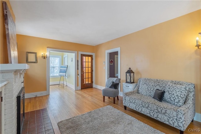 living room featuring a brick fireplace, baseboards, and wood finished floors