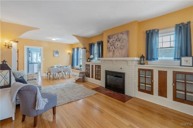 living area with baseboards, a fireplace, arched walkways, and wood finished floors