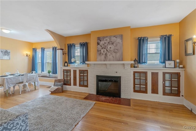 living area with a brick fireplace, wood finished floors, a wealth of natural light, and baseboards