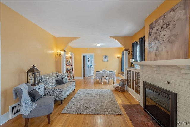 living area with arched walkways, a fireplace, visible vents, wood finished floors, and baseboards