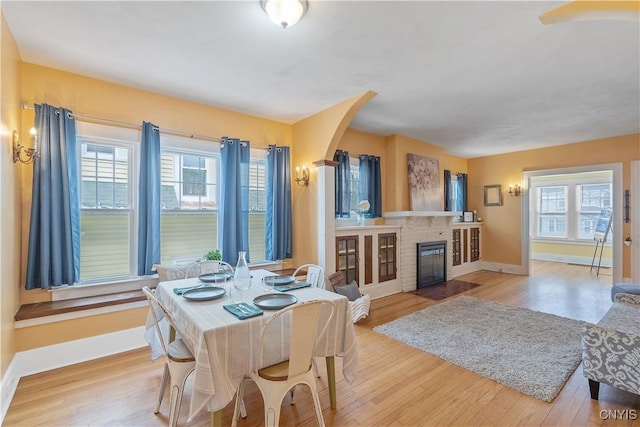 dining room with arched walkways, a brick fireplace, a healthy amount of sunlight, and wood finished floors