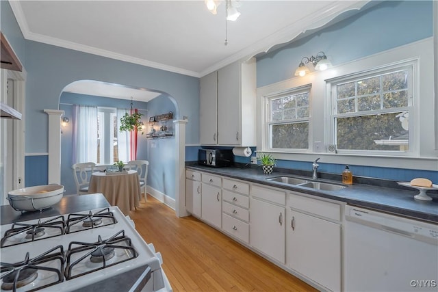 kitchen featuring white appliances, arched walkways, dark countertops, ornamental molding, and a sink