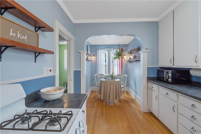 kitchen with arched walkways, open shelves, dark countertops, black microwave, and white gas range oven