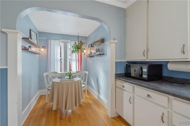 kitchen featuring arched walkways, light wood finished floors, dark countertops, white cabinetry, and black microwave