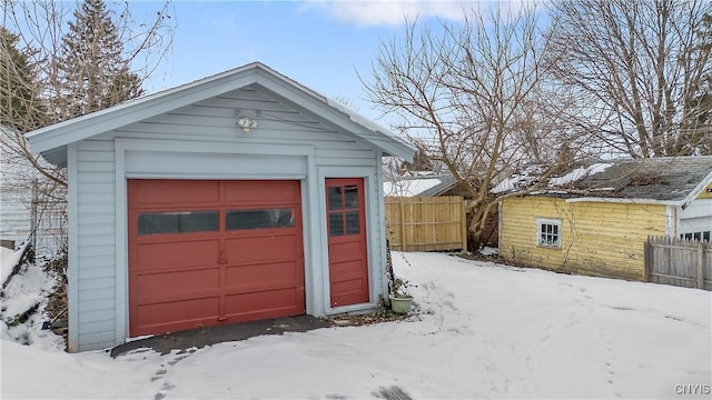 snow covered garage with a garage and fence