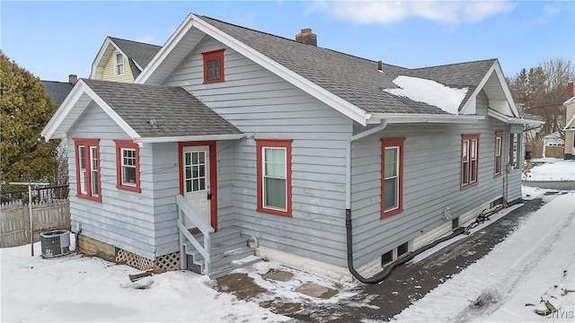 bungalow-style home featuring roof with shingles, a chimney, entry steps, central AC, and fence