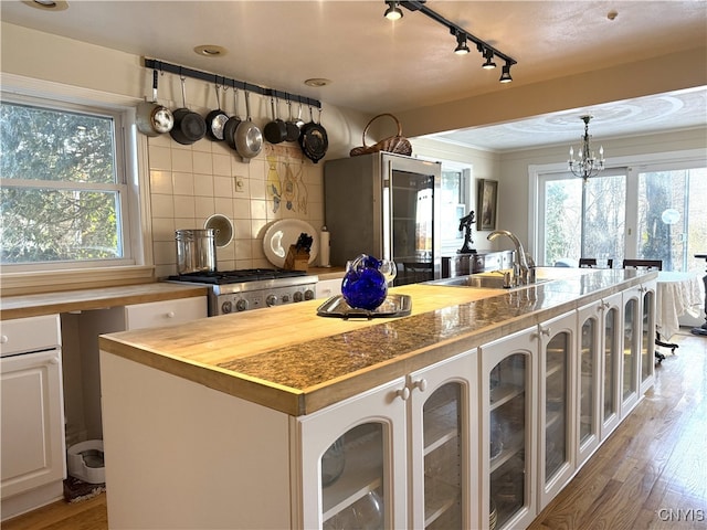 kitchen featuring stove, a sink, backsplash, refrigerator with glass door, and glass insert cabinets