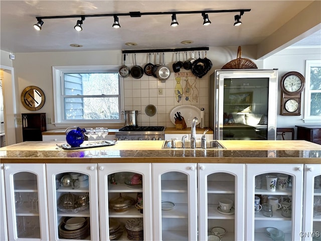 kitchen with tasteful backsplash, stove, glass insert cabinets, white cabinets, and a sink