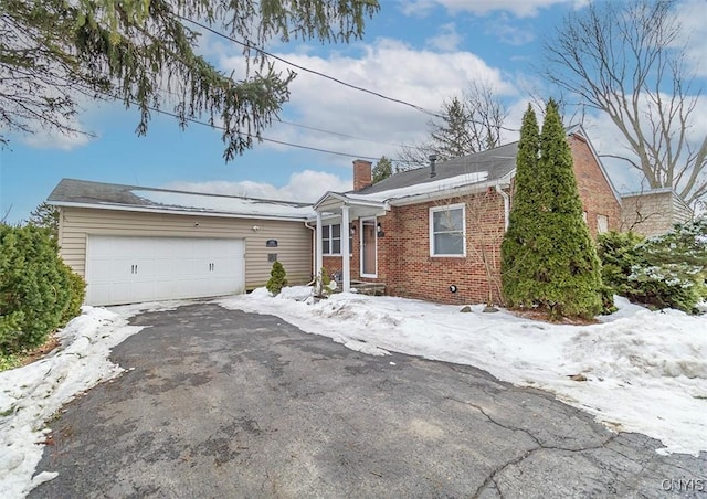 view of front of home featuring driveway, brick siding, a chimney, and an attached garage