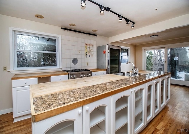 kitchen with light wood-style flooring, butcher block counters, stove, a sink, and decorative backsplash