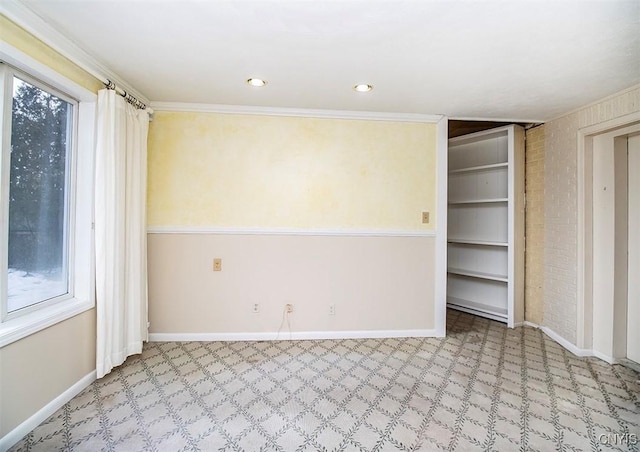 spare room featuring crown molding, brick wall, and baseboards