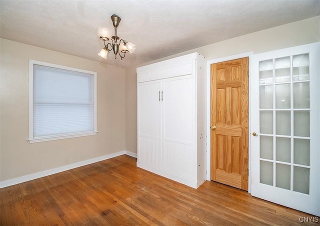 unfurnished bedroom featuring baseboards, a closet, wood finished floors, and a notable chandelier