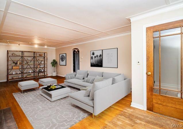 living area with arched walkways, crown molding, wood finished floors, baseboards, and track lighting