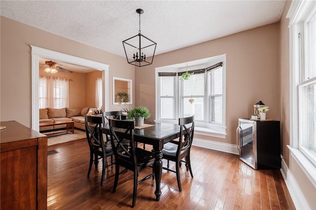 dining area with a notable chandelier, a textured ceiling, baseboards, and hardwood / wood-style flooring